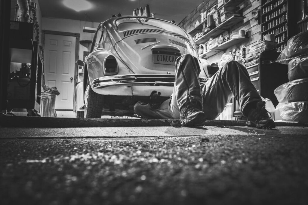 black and white car vehicle vintage 474 Mechanic working beneath a classic Volkswagen Beetle in a vintage garage setting.