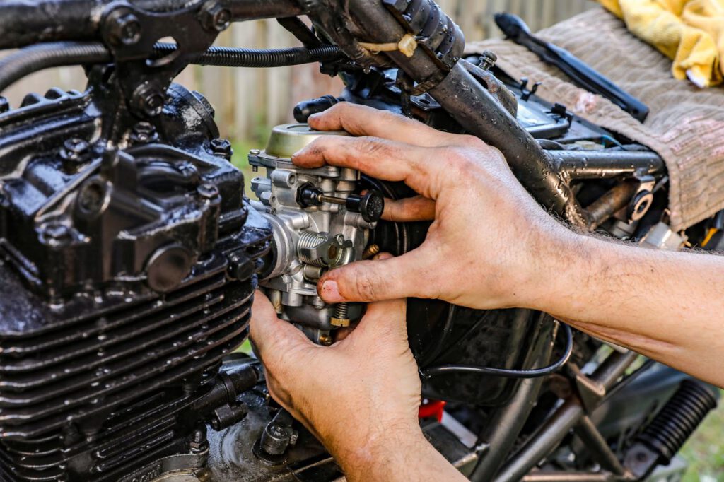 pexels photo 11890958 11890958 Close-up of a mechanic's hands assembling a motorcycle carburetor outdoors.