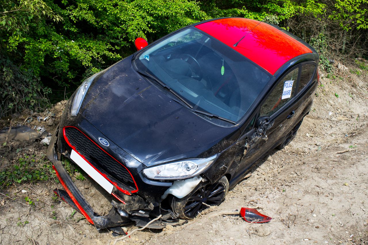 A black and red Ford Fiesta lies abandoned and damaged off-road in Welwyn Garden City, UK.