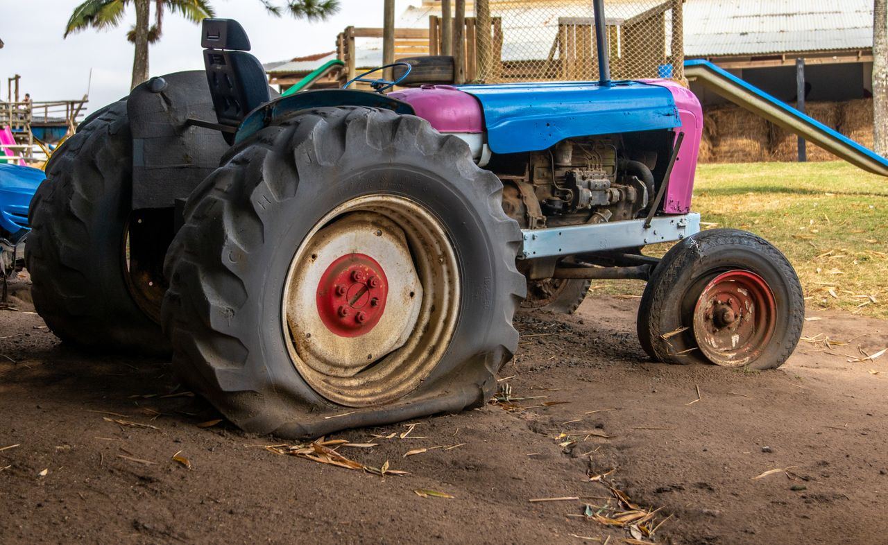 An old vintage tractor with flat tires parked on a rural farm setting.